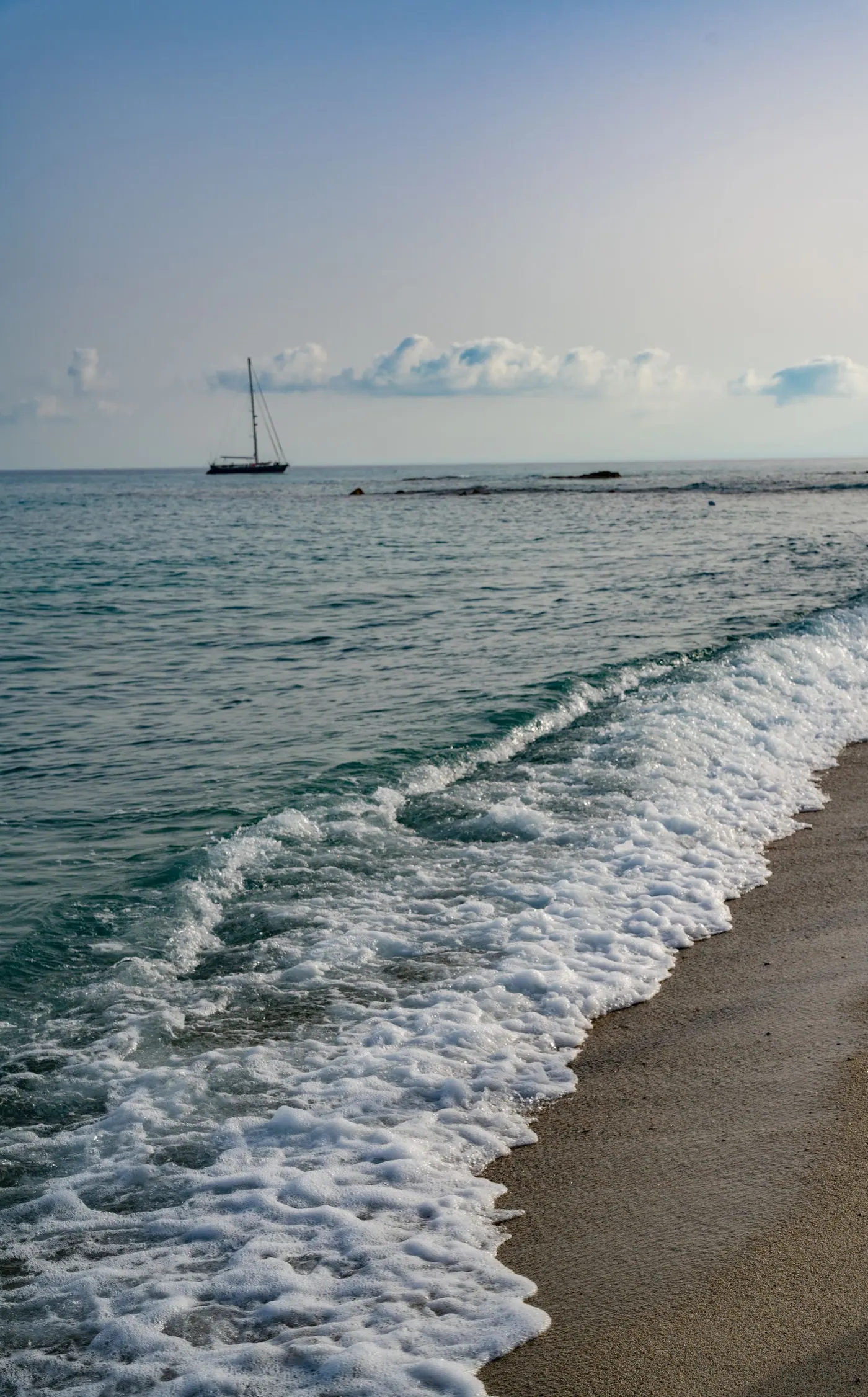 A sailboat beyond gentle waves on the Tropea coast